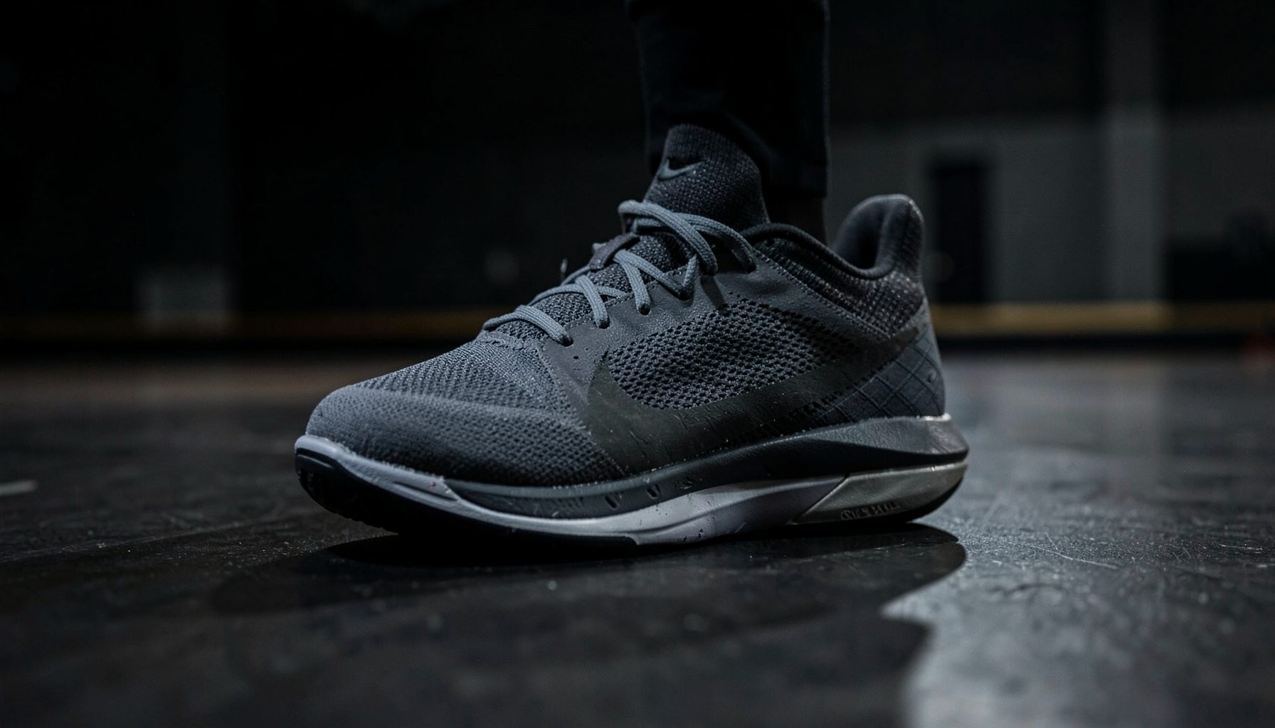 Nike Hyperdunk basketball shoe in dark gray, low-angle view against a shadowed gym floor
