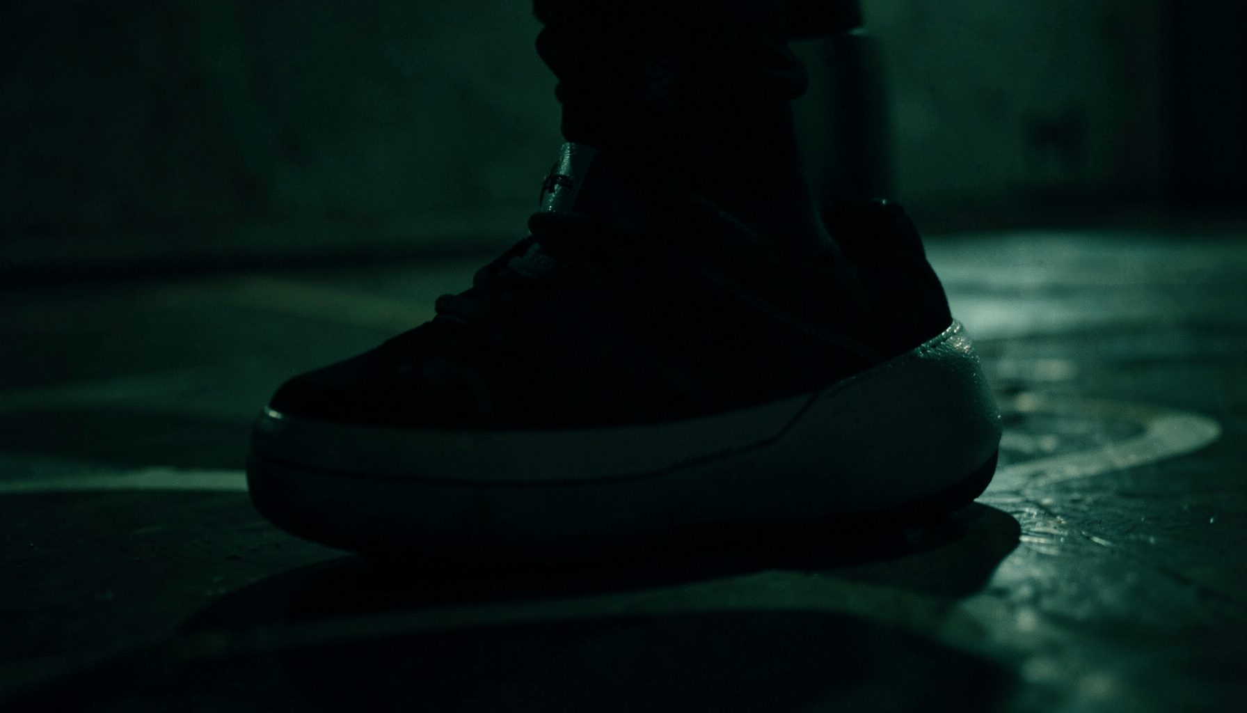 Dark atmospheric close-up of a basketball sneaker silhouette against a shadowy court background, moody green and black tones