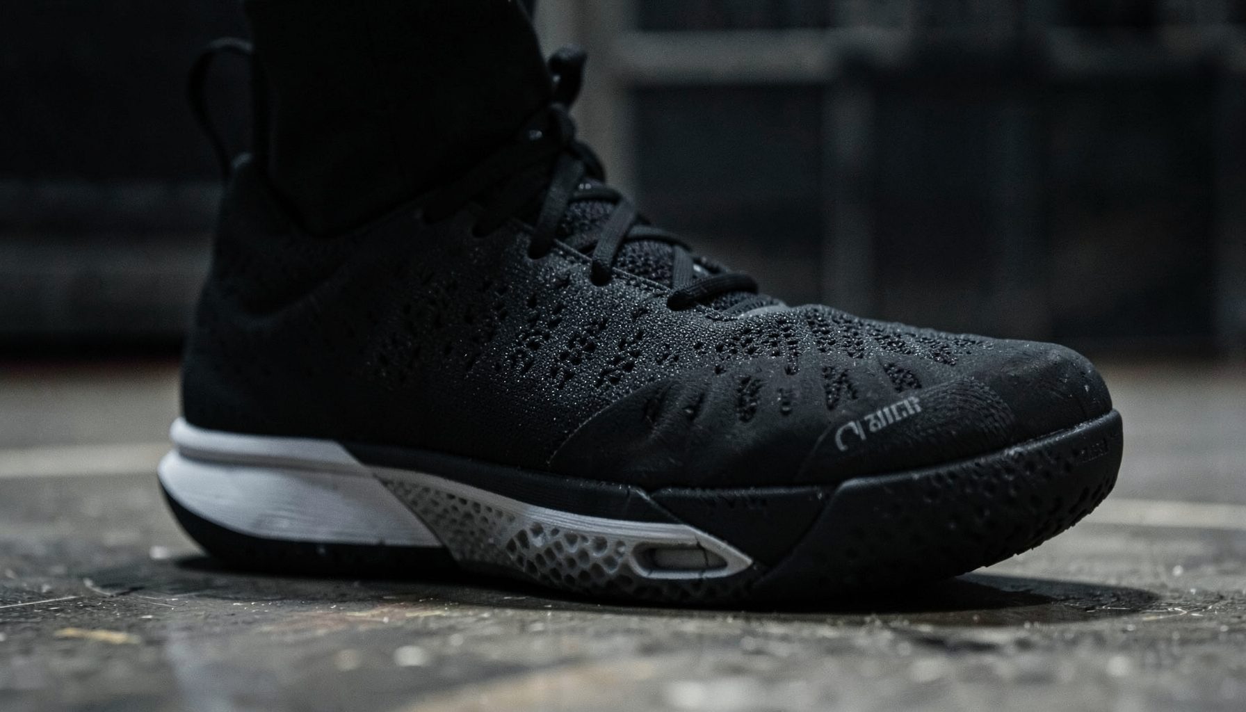 Close-up of a dark-toned men's basketball shoe with textured sole, moody lighting on a court surface