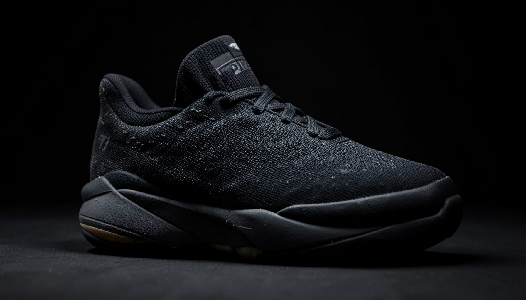 Close-up of a men's basketball shoe in dark tones with textured upper and visible cushioning, set against a shadowy studio backdrop