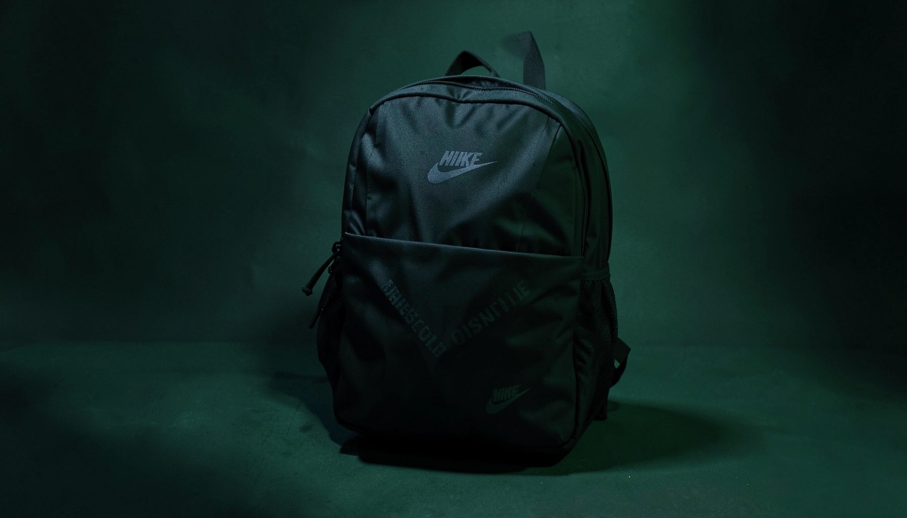 Dark Nike backpack with subtle branding, resting on a shadowed surface with moody green undertones