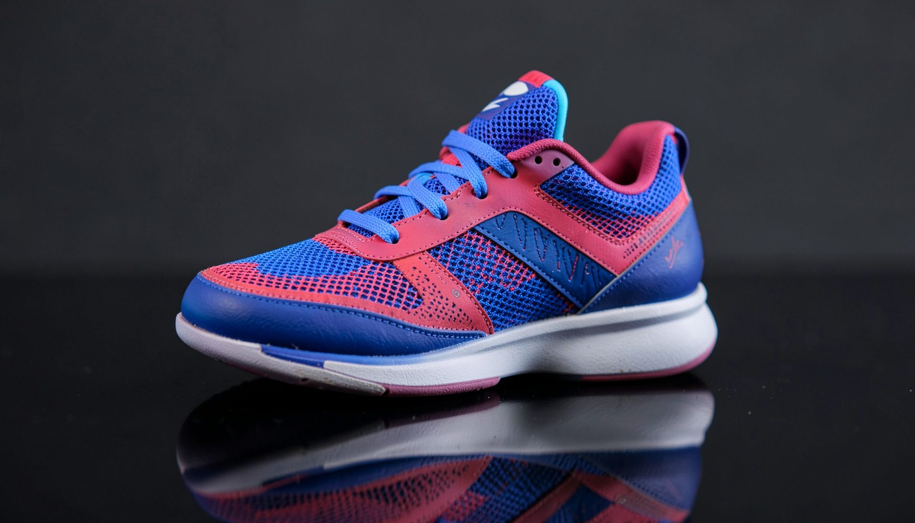 Youth-sized basketball sneaker in a bold colorway with mesh panels, resting on a dark reflective surface