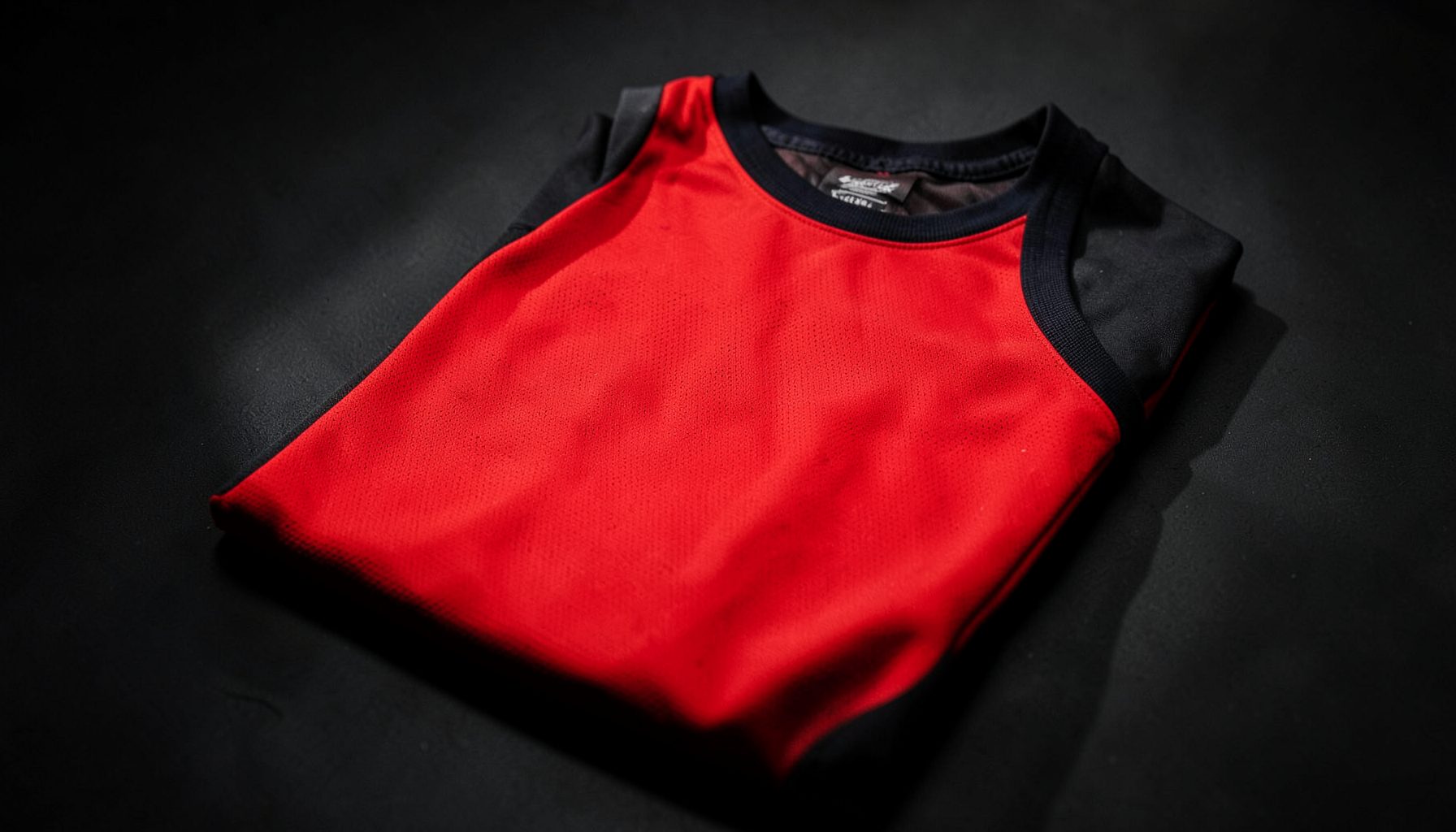 Red basketball throwback jersey with dark accents, folded on a shadowy surface